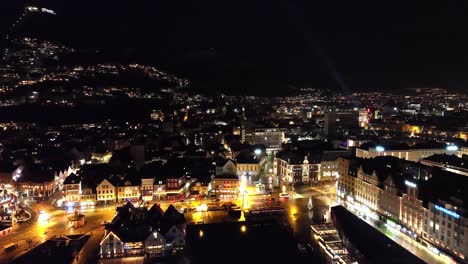 Antena-En-Movimiento-Hacia-Arriba-Desde-El-Mar-Cerca-Del-Mercado-De-Pescado-De-Bergen---Revelando-Una-Vista-Completa-De-La-Ciudad-Y-La-Ladera-Floyen-En-El-Fondo---Nochevieja-Con-Fuegos-Artificiales-Al-Azar-Exloding,-Noruega