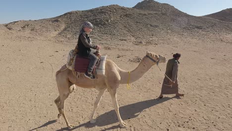 Hurgada,-Egypt-29-December-2022:-the-Camels-in-Sahara-Desert,-Egypt,-traditional-Dressed-Bedouins-Riding-Tourists-on-Camels-Through-Sandy-Desert