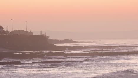 Weite-Sicht-Auf-Die-Wellen,-Die-Die-Küste-Von-Lissabon-Bei-Einem-Riesigen-Sonnenaufgang-Treffen