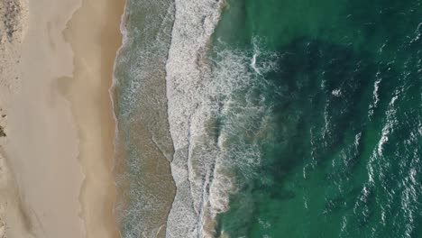 Top-down-drone-shot-of-waves-rolling-onto-the-beach-in-Tarifa,-Spain