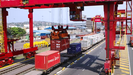 Toma-Aérea-De-Una-Grúa-De-Silla-De-Montar-Descargando-Un-Contenedor-De-Envío-De-Un-Tren