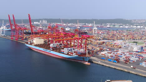 Wide-aerial-drone-shot-of-a-large-container-ship-being-loaded-by-gantry-cranes-Durban,-South-Africa