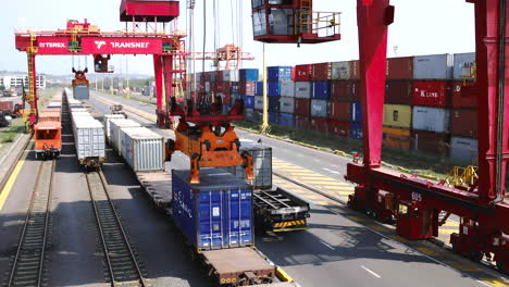 Aerial-drone-pullback-from-a-saddle-crane-removing-a-shipping-container-off-a-train-in-Durban-harbour