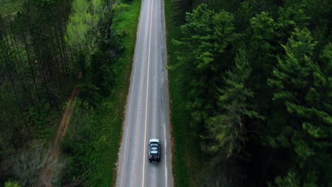 Aerial-Top-View-Flyover-of-Car-Driving-Through-Empty-Forest-Road-Surrounded-by-Trees