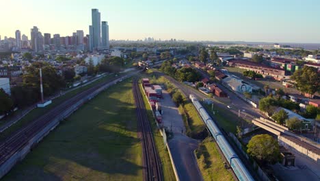Dolly-in-aerial-view-of-a-sustainable-transport,-long-range-electric-train-with-sunset-rays-on-the-side-in-Buenos-Aires,-Argentina