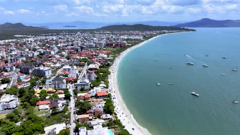 Aerial-drone-scene-of-hotel-complex-facing-the-sea-in-Florianópolis-tourist-beach-with-many-hotels-and-houses-facing-the-sea-in-Jurere-Internacional-and-beach-crowded-with-people