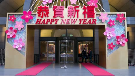 People-walk-into-a-building-displaying-a-celebrative-message,-Happy-New-Year,-for-the-Chinese-Lunar-New-Year-in-Hong-Kong