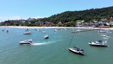 Low-flight-drone-aerial-scene-flying-over-speedboats-yachts-and-luxury-boats-with-pier-in-paradisiaca-beach-in-Canajurê-beach-florianopolis-santa-catarina-tropical