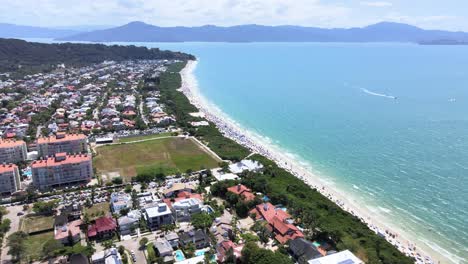 Drone-aerial-scene-of-beach-in-florianopolis-with-hotels-houses-and-buildings-facing-the-sea-with-many-accommodations-for-summer-season-and-sand-with-many-people-sunbathing-in-jurere-international