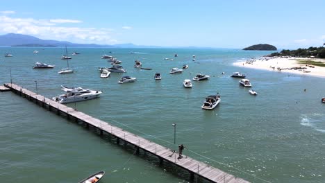 Low-flight-drone-aerial-scene-flying-over-speedboats-yachts-and-luxury-boats-with-pier-in-paradisiaca-beach-in-canajure-florianopolis-santa-catarina