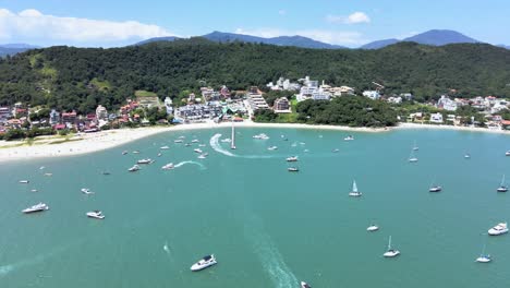 Aerial-scene-of-drone-flying-high-over-speedboats-yachts-and-luxury-boats-with-pier-on-paradisiaca-beach-in-canajure-beach-florianopolis-santa-catarina