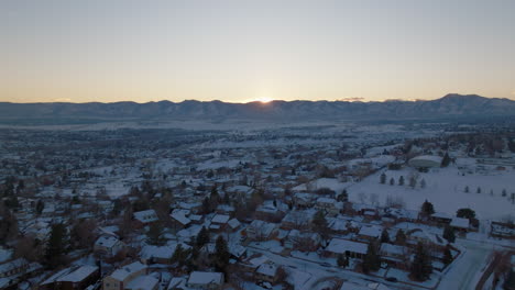 Drone-shot-of-the-sun-setting-over-the-Rocky-Mountains-in-Denver,-CO-on-a-snowy-winter-day