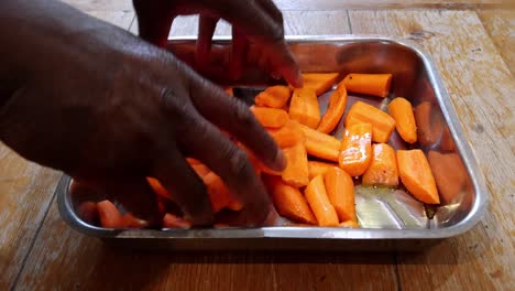 Cook-of-African-ethnicity-massaging-olive-oil-on-peeled,-cut-and-seasoned-carrots-ready-for-roasting