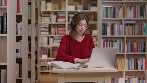 Junge-Frau-Setzt-Kopfhörer-Auf,-Während-Sie-Per-Laptop-In-Der-Bibliothek-Lernt