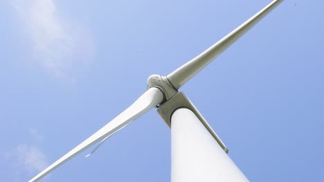 Below-wind-turbine-renewable-energy-generator-looking-up-at-spinning-blades-and-blue-sky