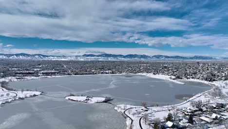 Aerial-drone-shot-circling-around-a-frozen-Sloan-Lake,-Denver-during-winter-storm-showing-Rocky-Mountains-in-background