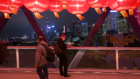 Ein-Mann-Fotografiert-Nachts-Von-Einer-Fußgängerbrücke-Aus-Die-Skyline-Von-Hong-Kong,-Während-Menschen-Während-Der-Feierlichkeiten-Zum-Chinesischen-Mondneujahrsfest-An-Ihm-Vorbeigehen