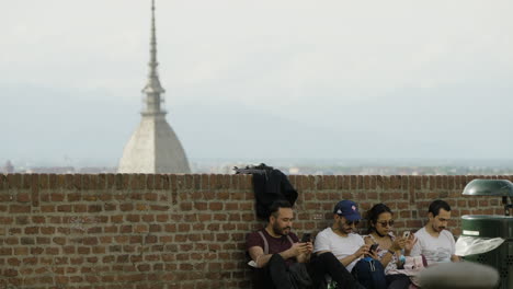 Touristen,-Die-Sich-An-Die-Wand-Lehnen,-Mit-Mole-Antonelliana-In-Turin,-Italien