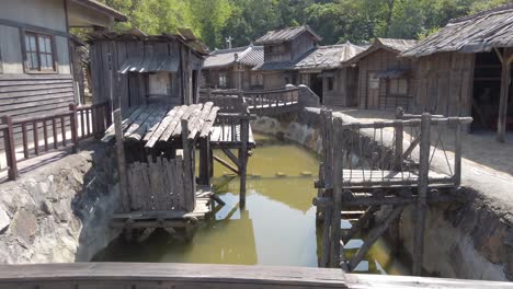 Caminando-Sobre-Un-Pequeño-Puente-Sobre-Un-Canal-Con-Casas-Tradicionales-En-Un-Pueblo-Coreano,-Una-Vieja-Película-Coreana-Ambientada-En-La-Ciudad-De-Suncheon,-Corea-Del-Sur