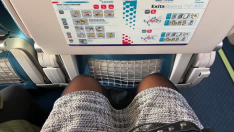 Viajando-En-Un-Asiento-De-Avión-Apretado-Con-Muy-Poco-Espacio-Para-Las-Piernas-En-Las-Aerolíneas-Luxair,-Piernas-Y-Rodillas-Femeninas-Apretadas-En-Un-Avión-Boeing,-Asiento-Incómodo,-Toma-De-4k