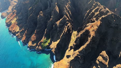 Aerial-View-of-Blue-Coastline-and-Crashing-Waves-along-Rolling-Hills-in-Kauai-Hawaii