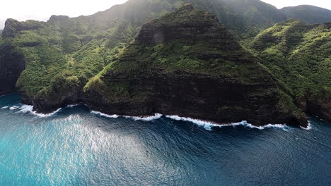 Vista-Aérea-De-La-Costa-Azul-Y-Las-Olas-Rompiendo-A-Lo-Largo-De-Las-Colinas-Ondulantes-En-Kauai-Hawaii