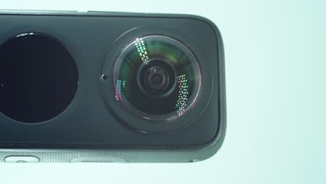 A-close-up-vertical-shot-of-a-360-camera-with-dual-lens,-two-lens-covers,-shiny-studio-lighting-reflecting,-round-screen,-turn-on-and-off-button,-on-a-rotating-stand,-slow-motion,-4K-video