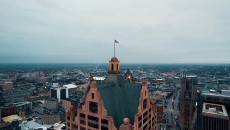 cinematic-aerial-of-us-Flag-on-top-of-The-Faison-Building-100-East,-milwaukee,-Wisconsin,-USA-captured-at-sunrise-on-a-cloudy-day