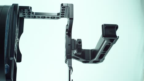 Eine-Vertikale-Nahaufnahme-Eines-Kamerakäfigs-Aus-Schwarzem-Metall-Mit-Einem-Handler-Darüber,-Videoproduktionsausrüstung,-Auf-Einem-Um-360-Drehbaren-Ständer,-Studiolicht,-Zeitlupe,-4k
