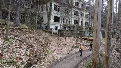 Aerial-of-urban-explorers-walking-around-the-property-of-an-abandoned-hopsital-building-in-Zagreb,-Croatia-