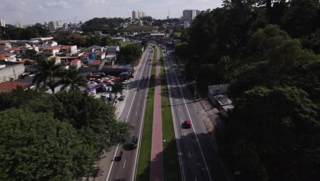 Drone-moves-straight-ahead-over-an-avenue-with-a-bike-lane-in-the-middle,-some-trees-at-the-side-and-buildings-of-São-Paulo-city-in-the-other-side