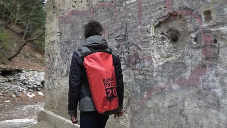 Man-touching-a-wall-with-gun-shot-wholes-of-an-abandoned-hospital-in-the-mountains-of-Sljeme,-Zagreb,-Croatia