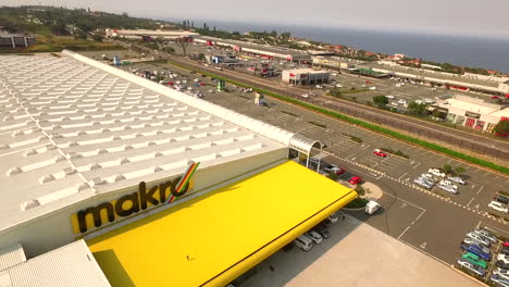 Toma-Aérea-De-Un-Dron-Del-Centro-Comercial-Makro-Con-El-Océano-De-Fondo