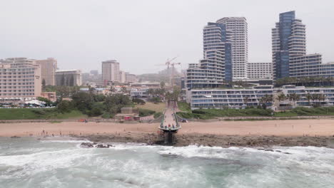 Aerial-drone-shot-of-Umhlanga-pier-and-the-Pearl-residences-in-Durban,-South-Africa-with-people-on-the-beach