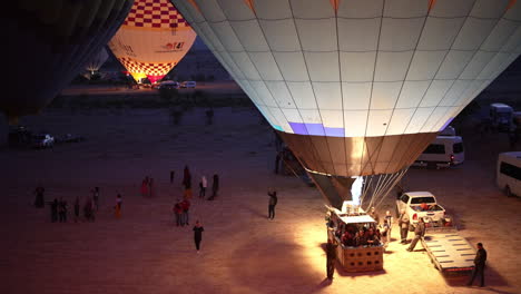 Hot-Air-Balloons-Preparing-For-Flight,-Flames-of-Burner-and-People-at-Night,-Aerial-View