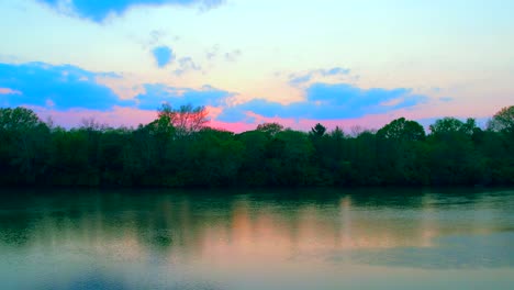Drone-flying-on-river-at-sunset-with-colorful-sky-in-background