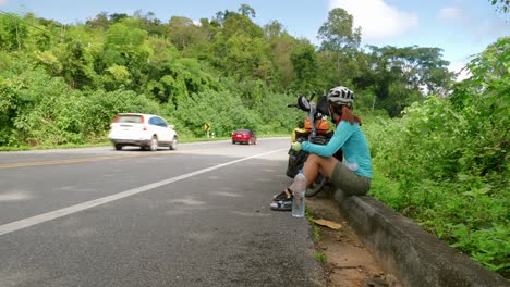 Asian-having-a-break-after-cycling-snacking-on-the-shoulder-of-a-Southeast-Asian-road