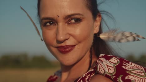 A-close-up-shot-of-the-face-of-an-attractive-carefree-Caucasian-female-with-feathers-in-her-hair-on-a-hot-summer's-day-outdoors