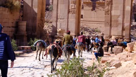 árabes-Montando-Burros-Sobre-Un-Camino-Empedrado-De-Piedra-A-Través-De-Petra-En-Jordania,-Oriente-Medio,-Con-Turistas-Explorando-La-Ciudad-Antigua