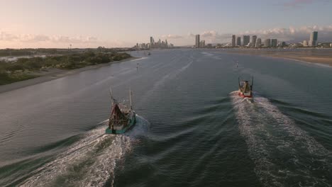 Aerial-view-over-two-fishing-trawlers-as-they-move-on-the-Broadwater-on-the-Gold-Coast-moving-towards-Surfers-Paradise,-Queensland,-Australia