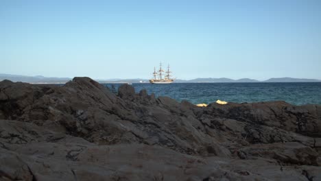 Low-angle-wide-view-of-rocky-coastline-with-Amerigo-Vespucci-ship-on-background