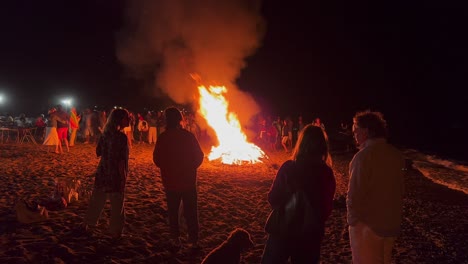 Gran-Multitud-En-El-Tradicional-Festival-De-Hogueras-En-La-Playa-En-La-Celebración-De-San-Juan-En-Marbella-España,-Gente-Bailando-Y-Disfrutando-De-Una-Divertida-Fiesta-Durante-El-Verano,-Gran-Fuego-Ardiente-Y-Llamas,-Tiro-De-4k