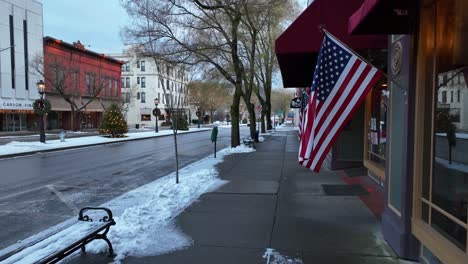 Low-aerial-glide-towards-American-flags-waving-on-snowy-day-in-small-town-in-America