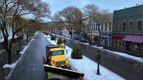 Schneepflug-Fahren-Auf-Wellsboro,-Pa-Hauptstraße-Gesäumt-Von-Weihnachtsdekorationen-Während-Des-Aktiven-Schneesturms-Im-Dezember,-Wunderschön-Beleuchtete-Weihnachtsbäume-Und-Geschäfte-In-Der-Amerikanischen-Stadt