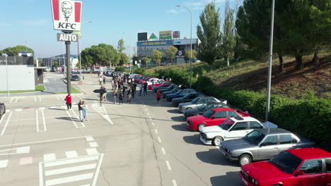 Vista-Aérea-Sobre-La-Fila-De-Autos-Bmw-Series-Classic-E30-Estacionados-En-Una-Reunión-De-Fans-En-El-Estacionamiento-Del-Restaurante-Kfc