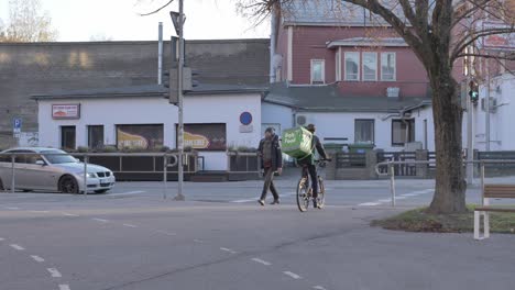 Bolt-food-courier-on-bicycle-is-passing-wolt-courier-on-foot-on-streets-of-Tartu