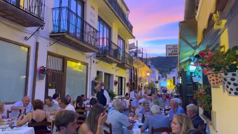 Gente-Sentada-Y-Cenando-Afuera-En-Un-Restaurante-Con-Un-Hermoso-Cielo-Rosado-Al-Atardecer-En-Benahavis-España,-Calle-Romántica-Por-La-Noche-Durante-El-Verano,-Tiro-De-4k