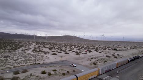 Drohnenaufnahmen-Aus-Der-Luft-Eines-Güterzugs-In-Der-Wüste-Von-Palm-Springs-Mit-Windparks-Im-Hintergrund,-Langsame-Bewegung-Nach-Vorne