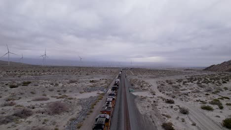 Aerial-Drone-Footage-of-Cargo-Train-in-Palm-Springs-Desert-with-Wind-Farms-in-the-Background,-slow-moving-shot