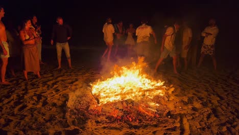 Gente-Saltando-Sobre-Una-Hoguera-Tradicional-En-El-Festival-De-San-Juan-En-La-Playa-De-Marbella-España,-Amigos-Y-Familiares-Disfrutando-De-Una-Fiesta-Divertida,-Saltando-Sobre-Un-Fuego-Ardiente-Y-Llamas-Calientes-Por-La-Noche,-Tiro-De-4k